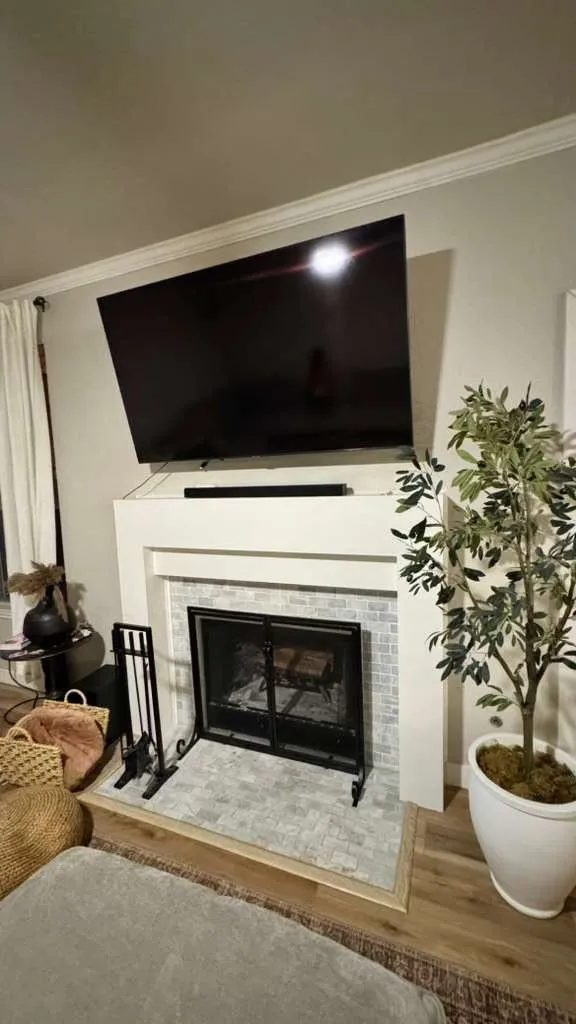 After: refreshed fireplace with a new white surround, tile hearth, and television mounted above